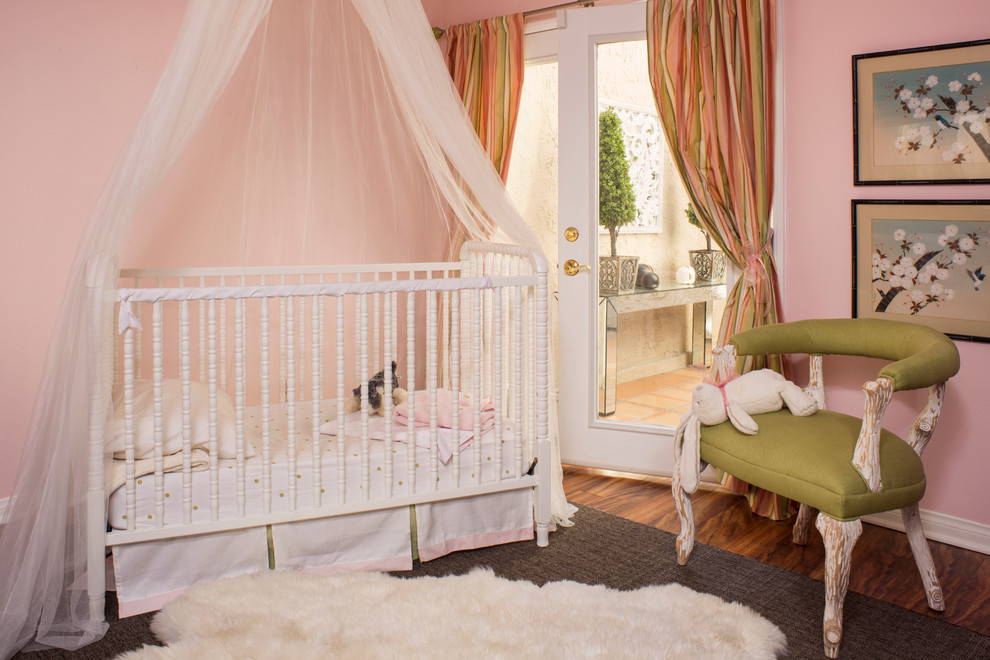 Cette photo montre une petite chambre de bébé fille chic avec un mur rose et un sol en bois brun.