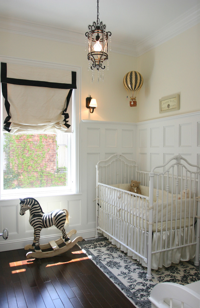 Cette photo montre une chambre de bébé neutre chic de taille moyenne avec parquet foncé et un mur jaune.