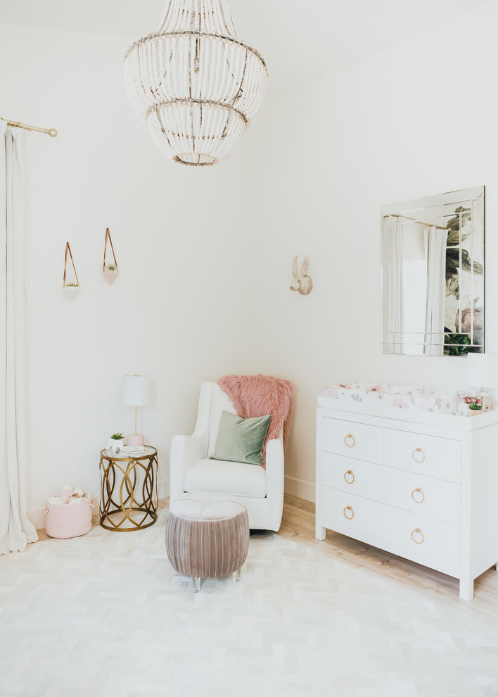 Design ideas for a small traditional nursery for girls in Los Angeles with white walls and light hardwood flooring.