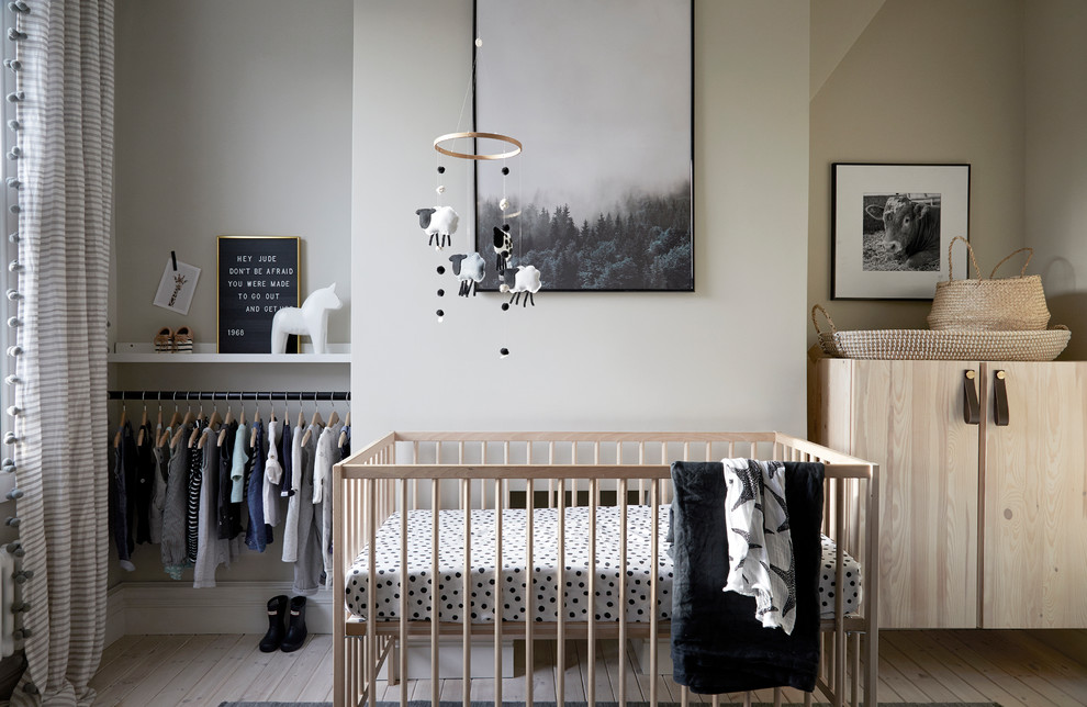 Photo of a small scandinavian gender neutral nursery in London with white walls, light hardwood flooring and beige floors.