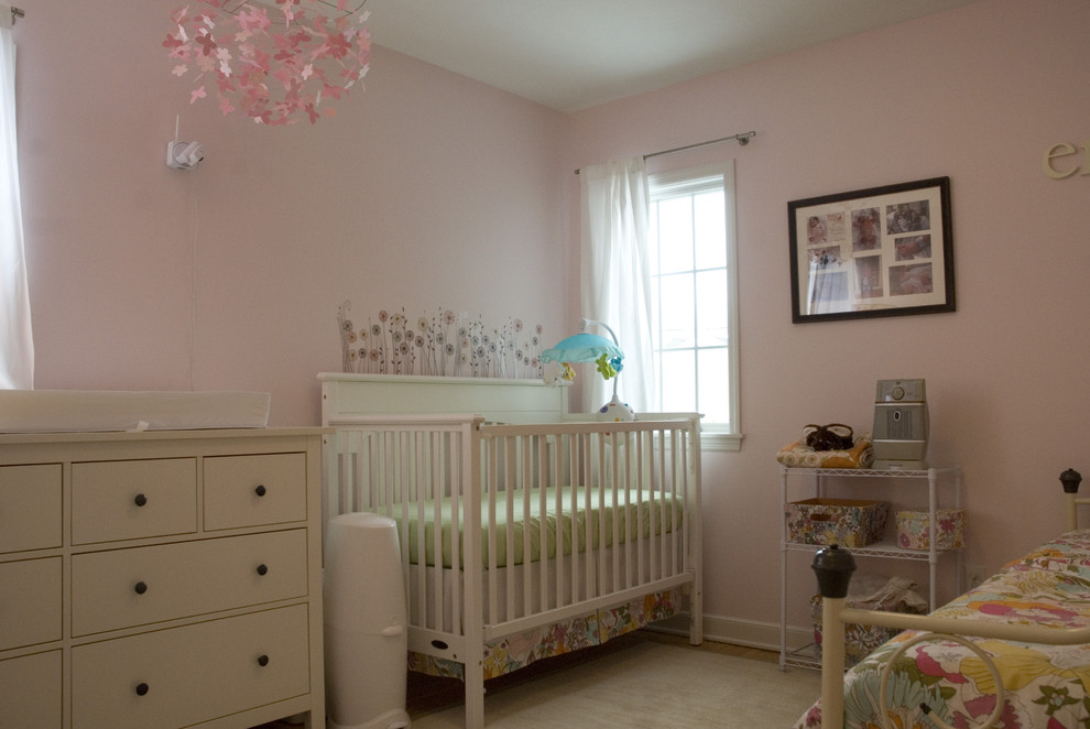 Foto de habitación de bebé niña clásica renovada pequeña con paredes rosas, suelo de madera en tonos medios y suelo marrón