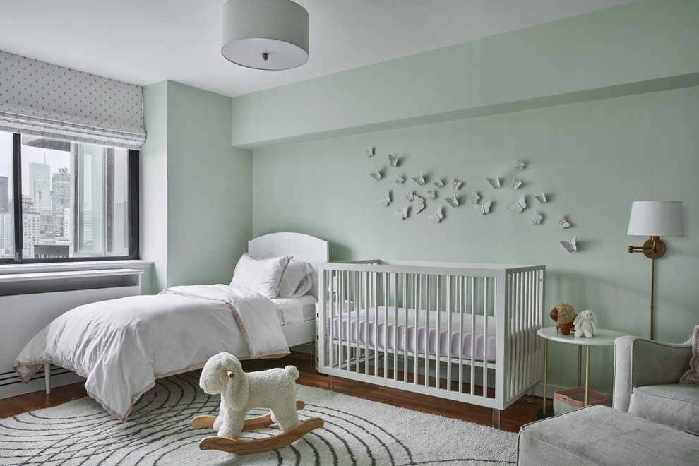 Cette image montre une chambre de bébé design avec un mur vert, un sol en bois brun et un sol marron.
