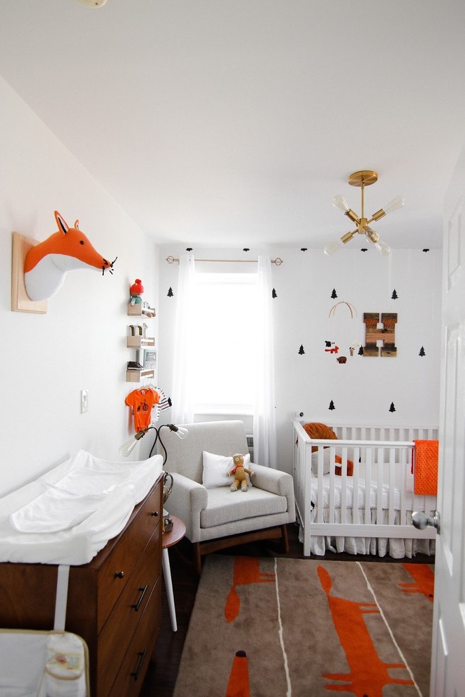 Esempio di una piccola cameretta per neonati neutra contemporanea con pareti bianche, pavimento in legno massello medio e pavimento marrone