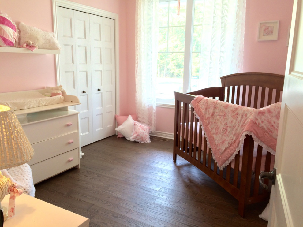 Diseño de habitación de bebé niña tradicional de tamaño medio con paredes rosas y suelo de madera en tonos medios