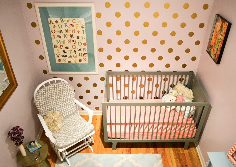 Immagine di una piccola cameretta per neonata moderna con pareti viola e pavimento in legno massello medio