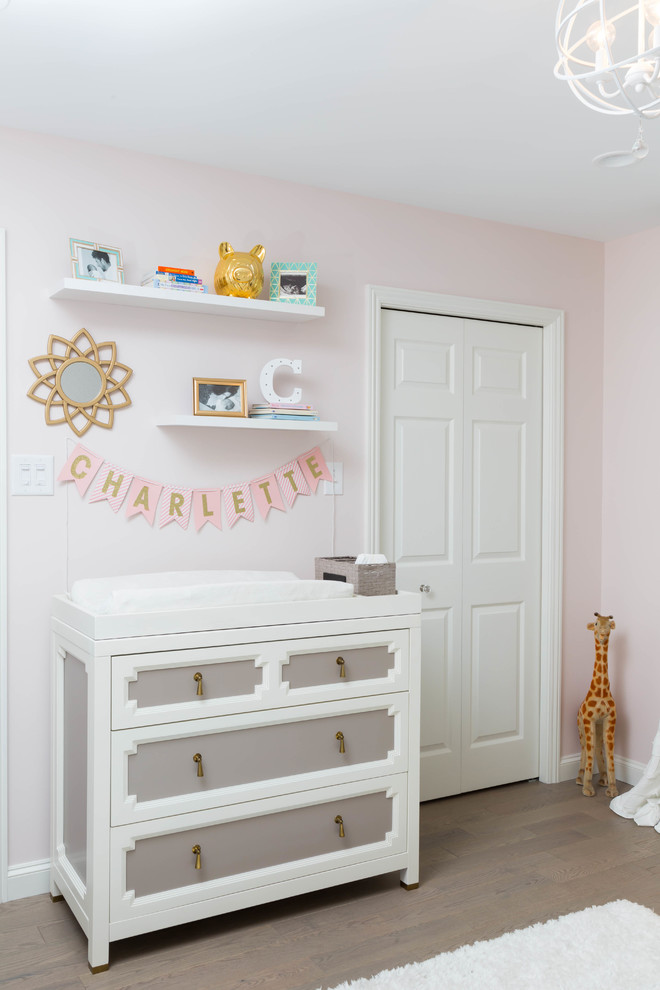 Foto di una cameretta per neonata minimalista con pareti rosa e parquet chiaro