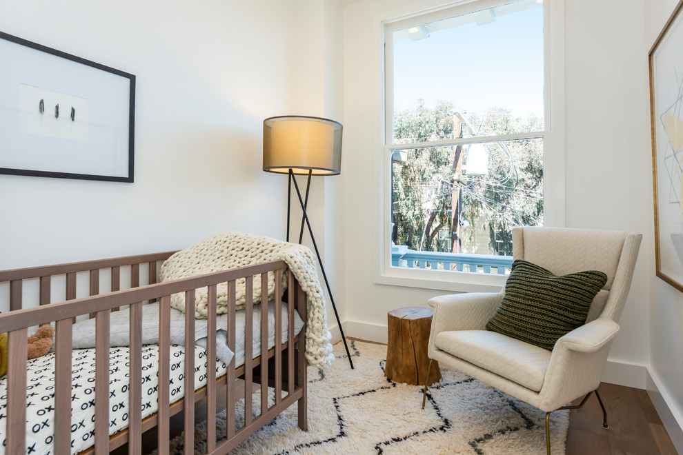 Cette image montre une petite chambre de bébé neutre design avec un mur blanc, un sol en bois brun et un sol marron.