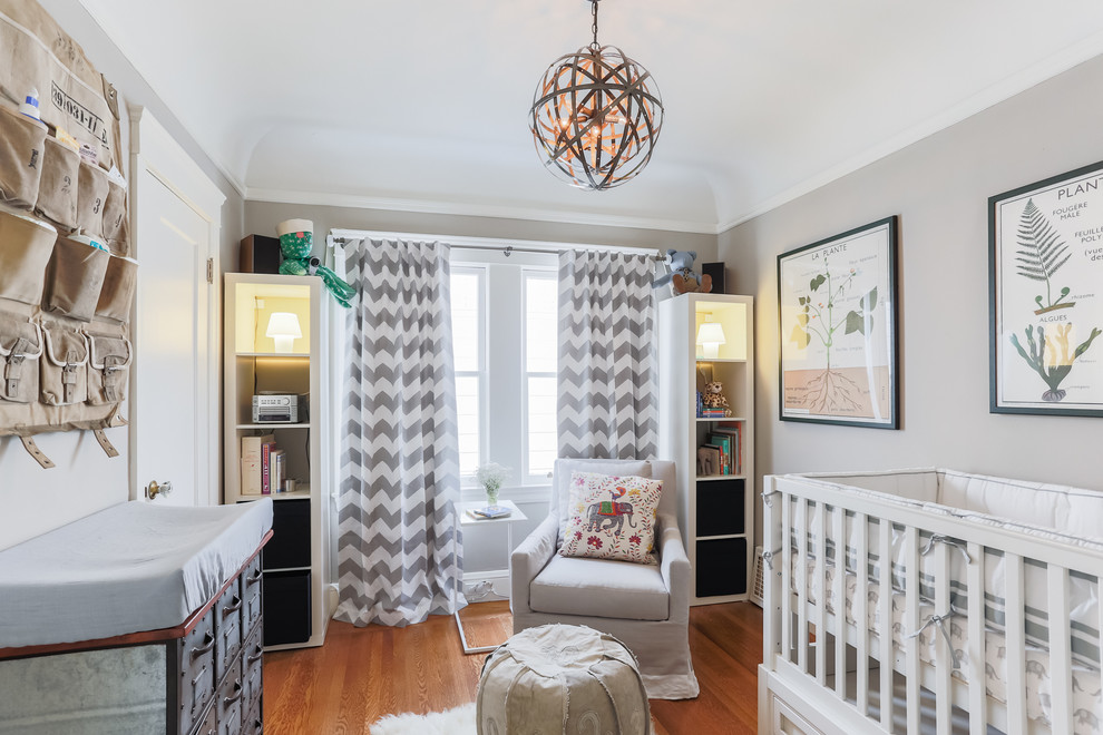 Diseño de habitación de bebé neutra clásica renovada de tamaño medio con paredes grises, suelo de madera en tonos medios y suelo naranja