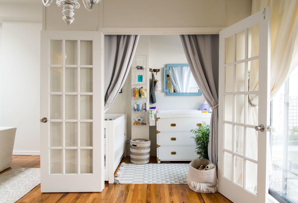 Modelo de habitación de bebé neutra tradicional renovada pequeña con paredes beige y suelo de madera en tonos medios