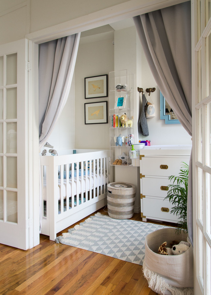 Diseño de habitación de bebé neutra clásica renovada pequeña con paredes beige y suelo de madera en tonos medios