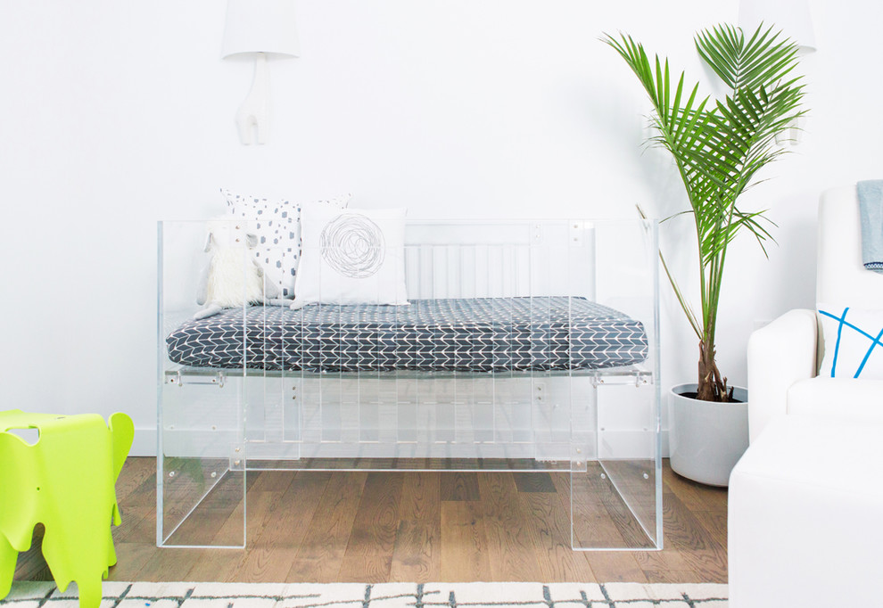 Immagine di una cameretta per neonato minimalista di medie dimensioni con pareti bianche e pavimento in legno massello medio