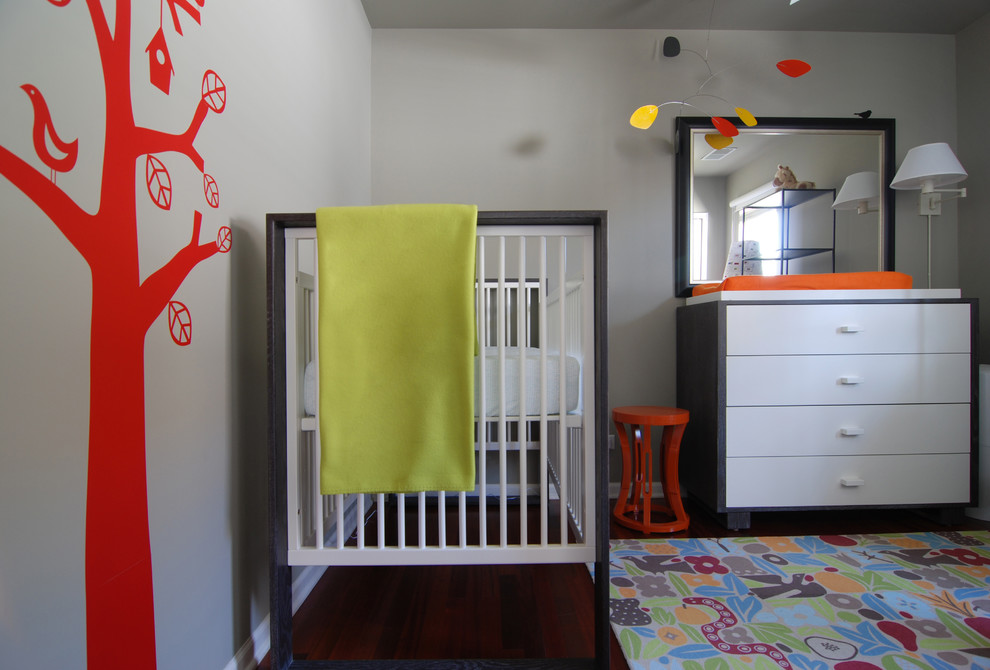 This is an example of a modern gender neutral nursery in Los Angeles with grey walls and dark hardwood flooring.