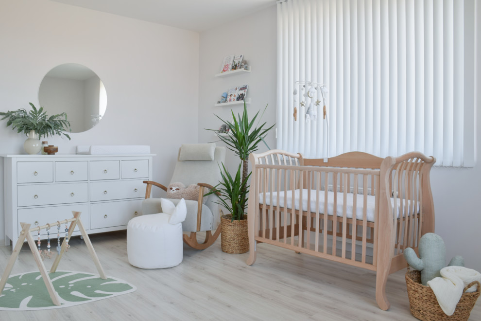Esempio di una piccola cameretta per neonati neutra moderna con pareti bianche e parquet chiaro