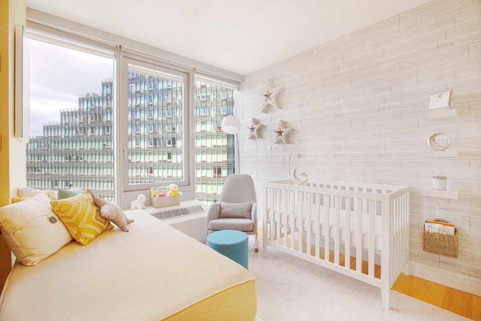 Modelo de habitación de bebé neutra actual pequeña con paredes grises, suelo de madera clara y suelo marrón