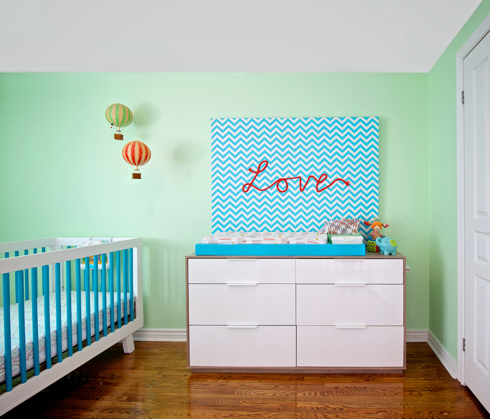 Exemple d'une petite chambre de bébé tendance avec un mur vert et un sol en bois brun.