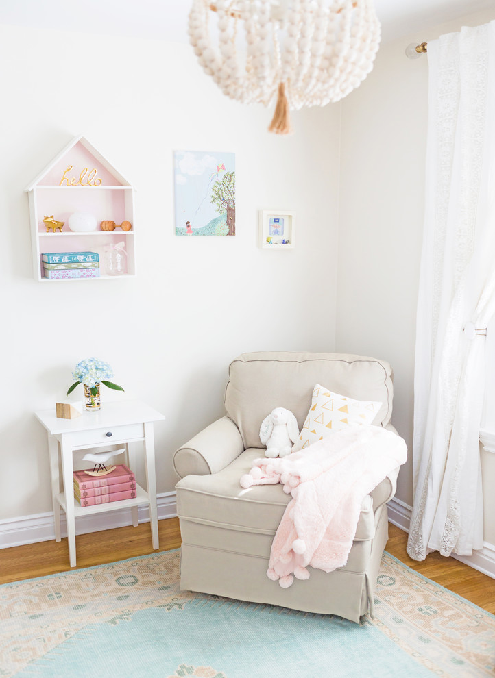 Photo of a small eclectic nursery for girls in Los Angeles with beige walls and light hardwood flooring.
