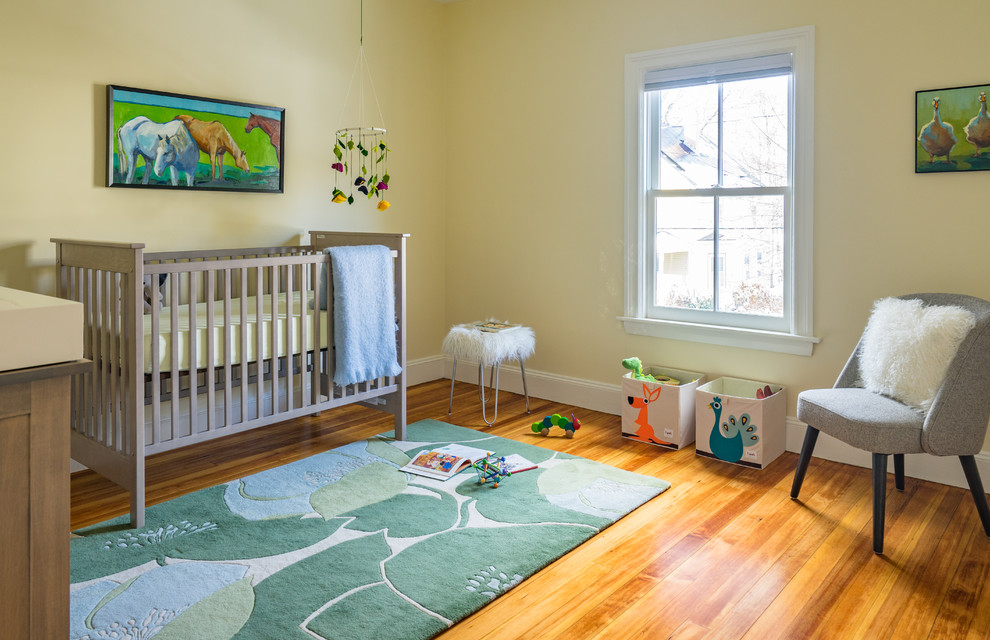 Ejemplo de habitación de bebé neutra tradicional renovada con paredes amarillas, suelo de madera en tonos medios y suelo marrón