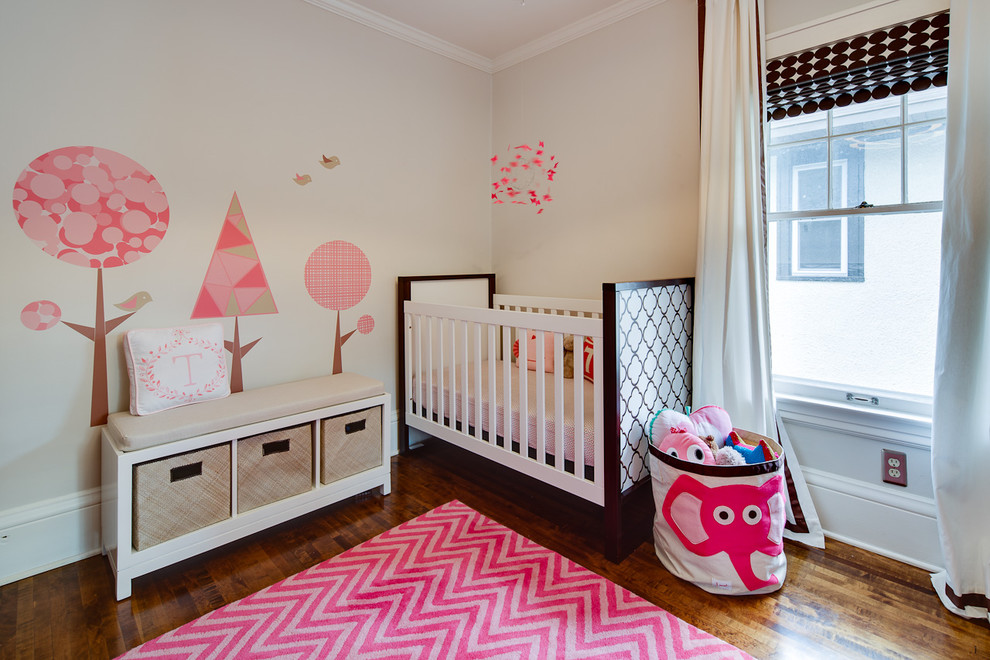 Modelo de habitación de bebé niña tradicional renovada con paredes beige y suelo de madera oscura