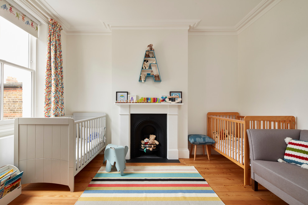 Photo of a large traditional gender neutral nursery in London with white walls, medium hardwood flooring, multi-coloured floors and a chimney breast.