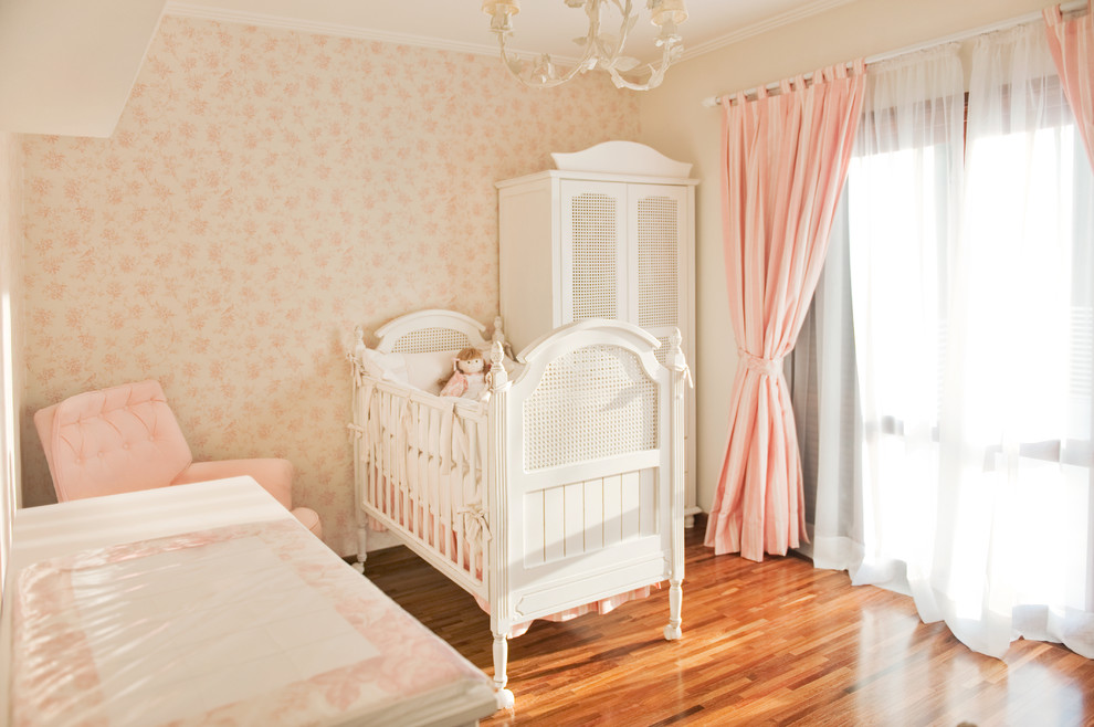 Ejemplo de habitación de bebé niña tradicional de tamaño medio con paredes rosas y suelo de madera en tonos medios