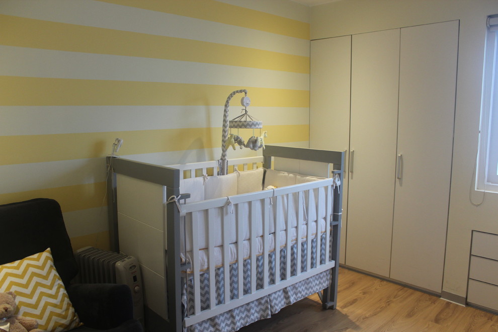 Exemple d'une petite chambre de bébé neutre chic avec un mur jaune, un sol en bois brun et un sol marron.