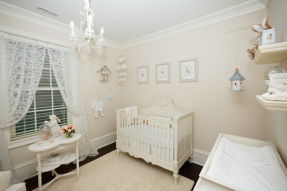 Modelo de habitación de bebé niña tradicional renovada de tamaño medio con paredes beige y suelo de madera oscura