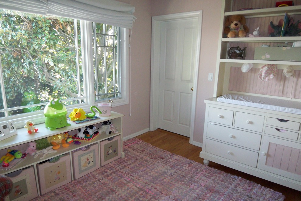 Imagen de habitación de bebé niña clásica con paredes rosas y suelo de madera en tonos medios