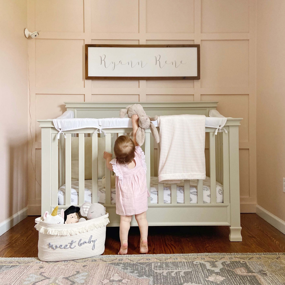 Réalisation d'une petite chambre de bébé fille champêtre avec un mur rose et un sol en bois brun.