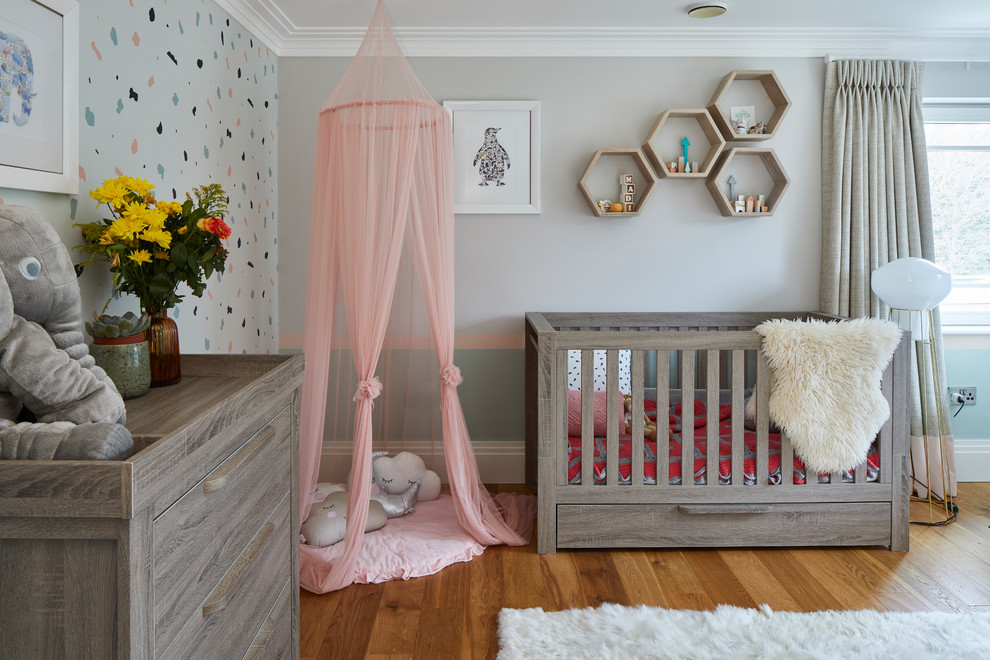 Ejemplo de habitación de bebé niña actual grande con paredes multicolor, suelo de madera en tonos medios y suelo marrón