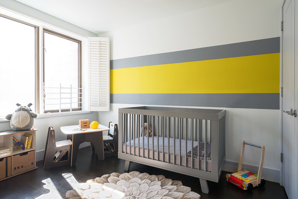 Aménagement d'une chambre de bébé neutre contemporaine avec un mur multicolore et parquet foncé.