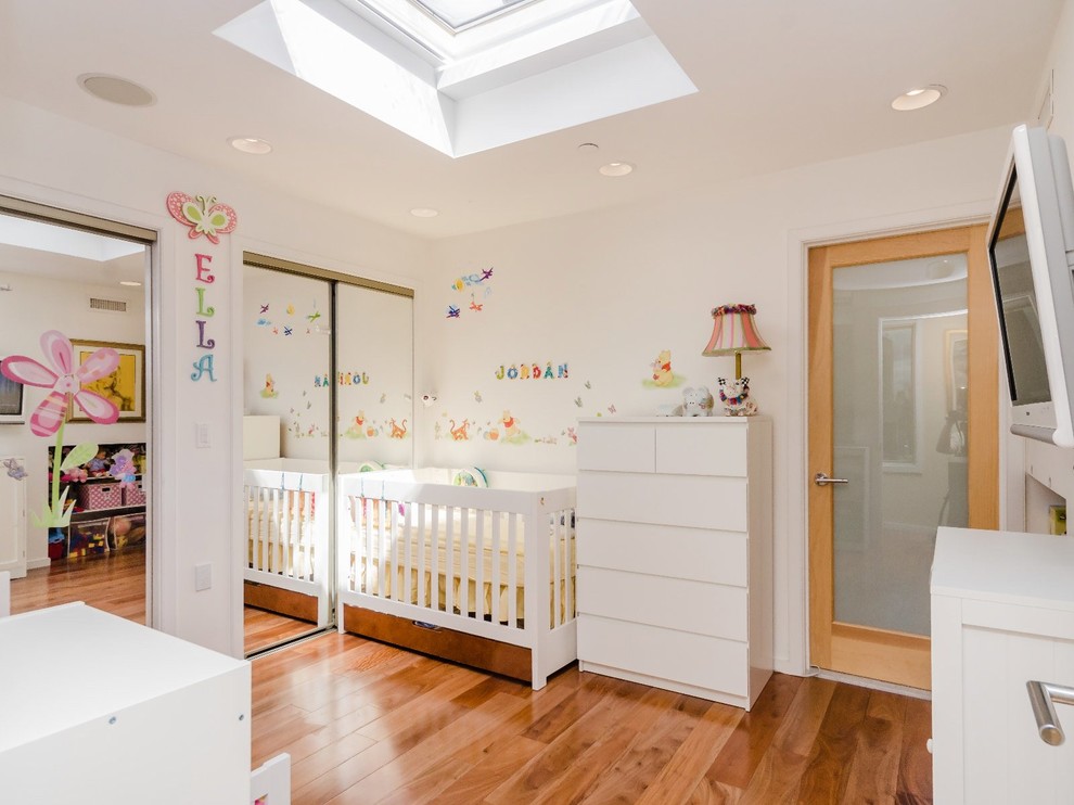 На фото: нейтральная комната для малыша среднего размера в современном стиле с белыми стенами и паркетным полом среднего тона с