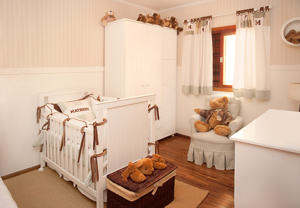 Modelo de habitación de bebé neutra moderna de tamaño medio con paredes beige y suelo de madera en tonos medios