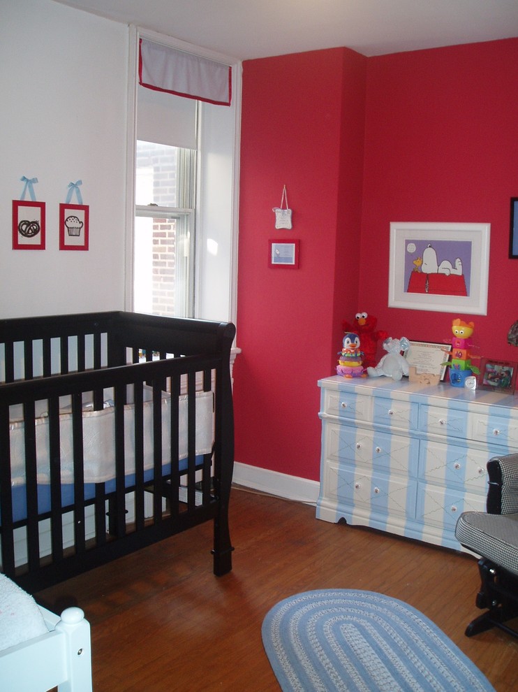 Ejemplo de habitación de bebé neutra contemporánea con paredes rojas y suelo de madera en tonos medios