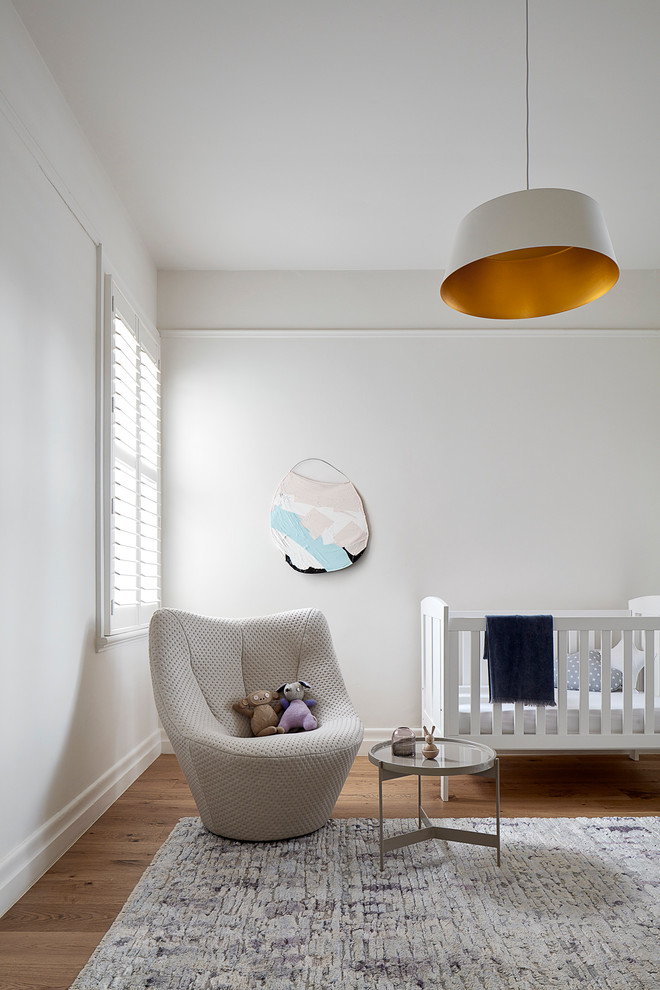 Modern gender neutral nursery in Melbourne with white walls, medium hardwood flooring, brown floors and feature lighting.