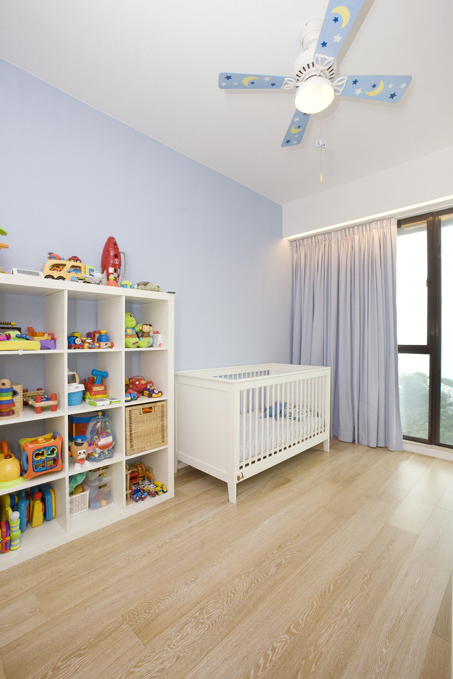 Ejemplo de habitación de bebé neutra actual con paredes azules y suelo de madera clara