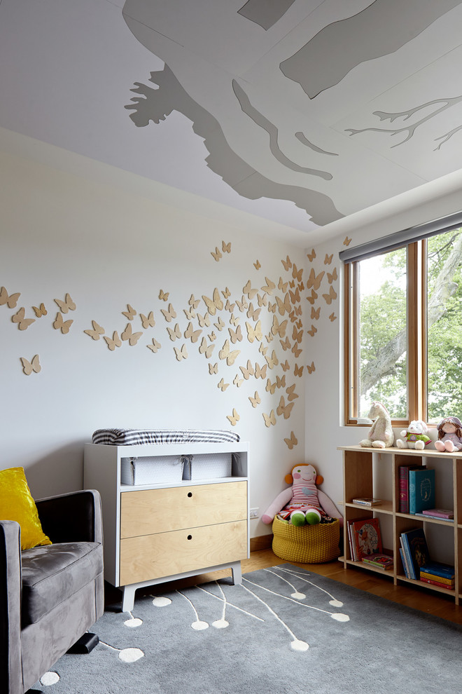 Photo of a contemporary nursery for girls in Kansas City with white walls, light hardwood flooring and brown floors.