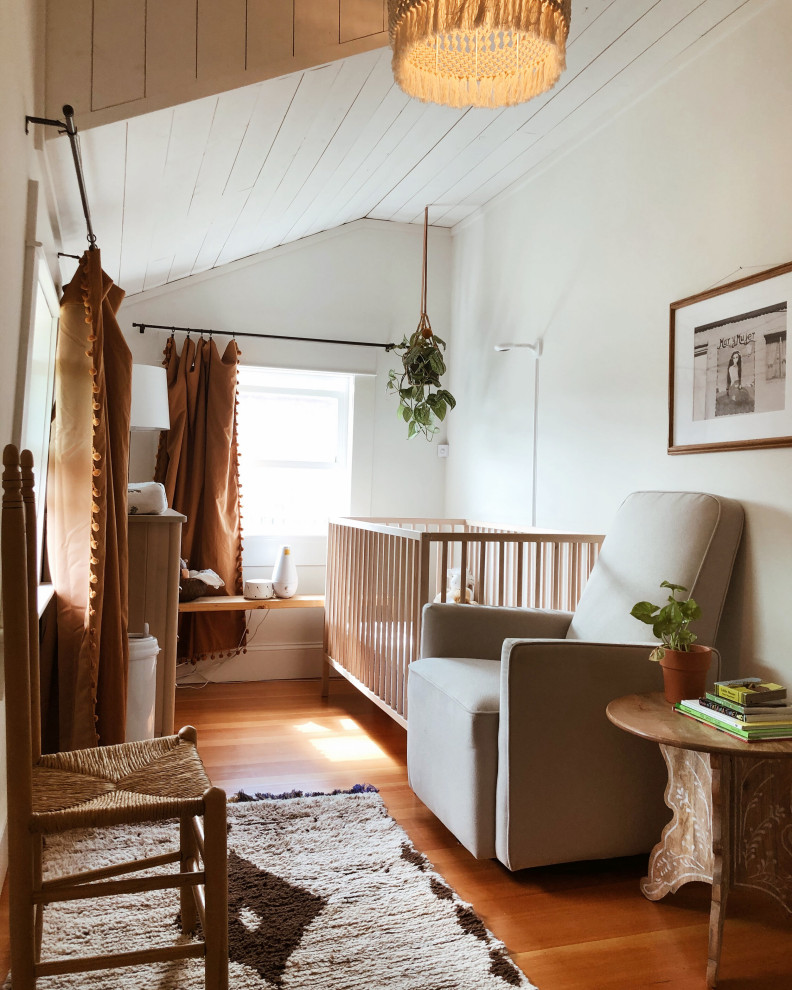 Foto di una piccola cameretta per neonata eclettica con pareti bianche, pavimento in legno massello medio, pavimento marrone e soffitto in perlinato