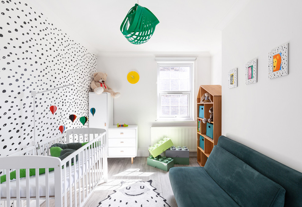 This is an example of a medium sized scandinavian gender neutral nursery in London with multi-coloured walls, light hardwood flooring, grey floors and wallpapered walls.