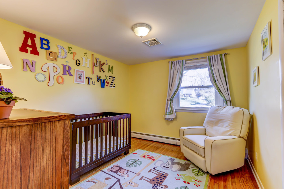 Modelo de habitación de bebé neutra clásica pequeña con paredes amarillas y suelo de madera en tonos medios
