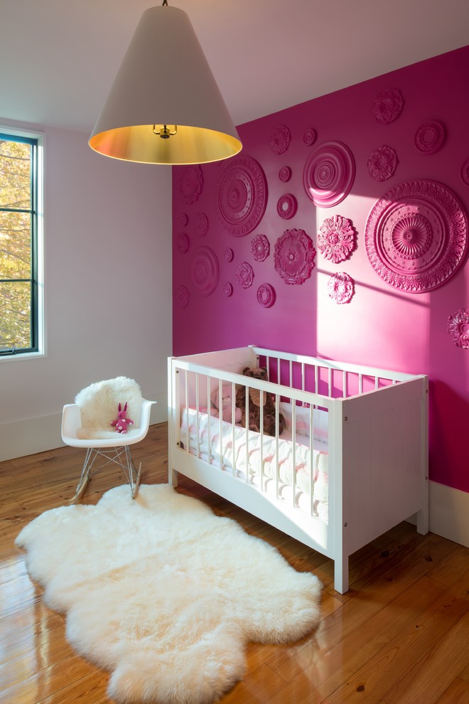 Modern inredning av ett babyrum, med rosa väggar och mellanmörkt trägolv