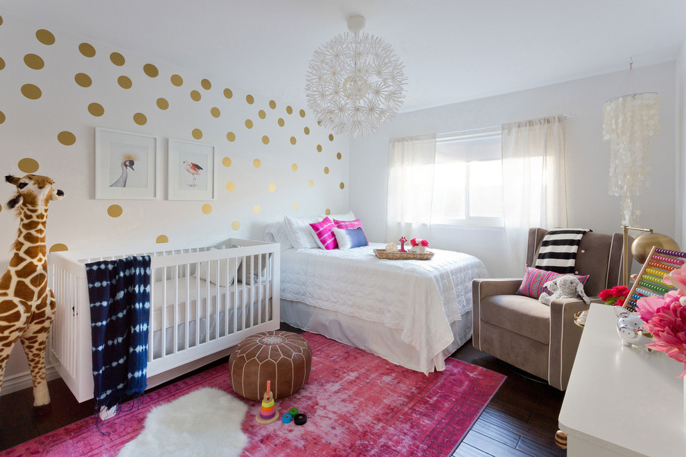 This is an example of a small eclectic nursery for girls in Los Angeles with white walls, laminate floors and brown floors.