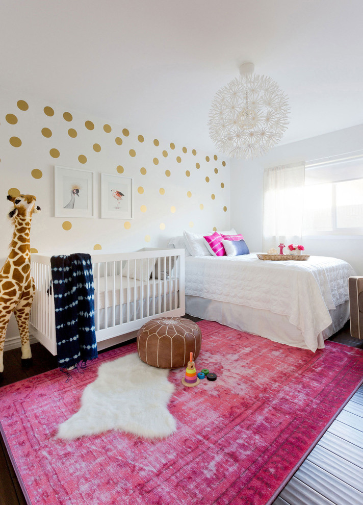 Small eclectic nursery for girls in Los Angeles with white walls, laminate floors and brown floors.