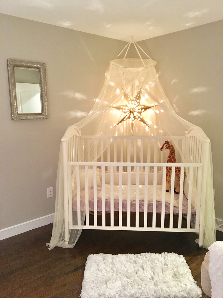 Modelo de habitación de bebé niña clásica renovada de tamaño medio con paredes grises, suelo de madera oscura y suelo marrón