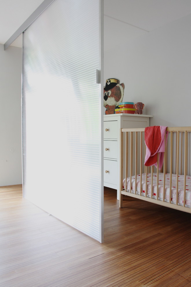 Diseño de habitación de bebé neutra actual con paredes blancas y suelo de madera en tonos medios