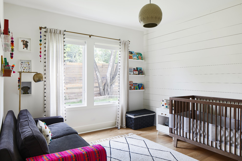 Modelo de habitación de bebé neutra clásica renovada de tamaño medio con paredes blancas, suelo de madera en tonos medios y suelo marrón