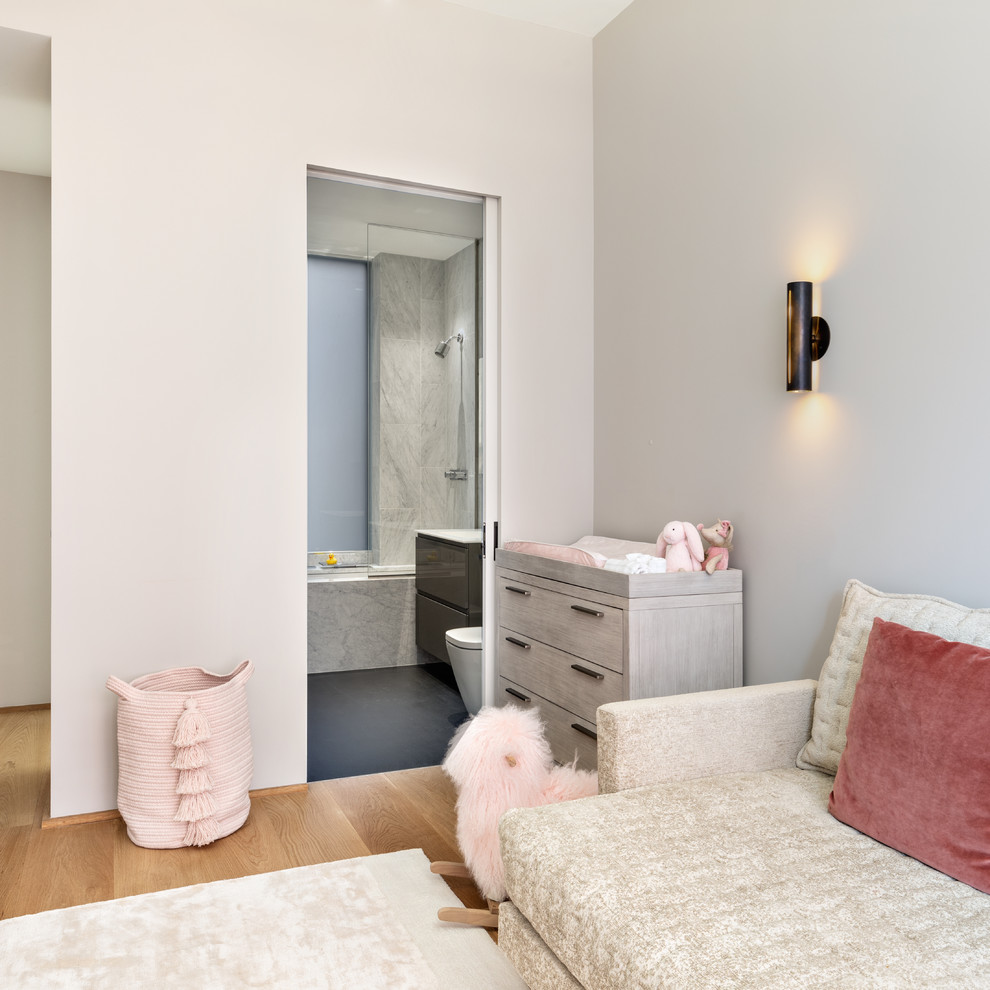 Ejemplo de habitación de bebé niña actual de tamaño medio con paredes rosas, suelo de madera clara y suelo beige