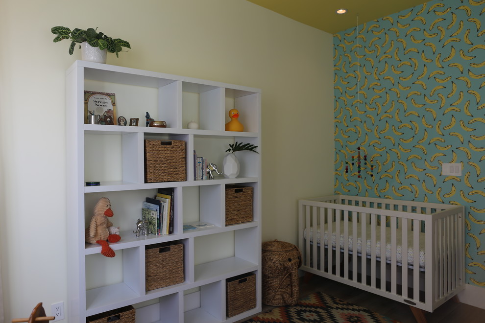 Idée de décoration pour une grande chambre de bébé neutre avec un mur jaune, un sol en bois brun et un sol marron.