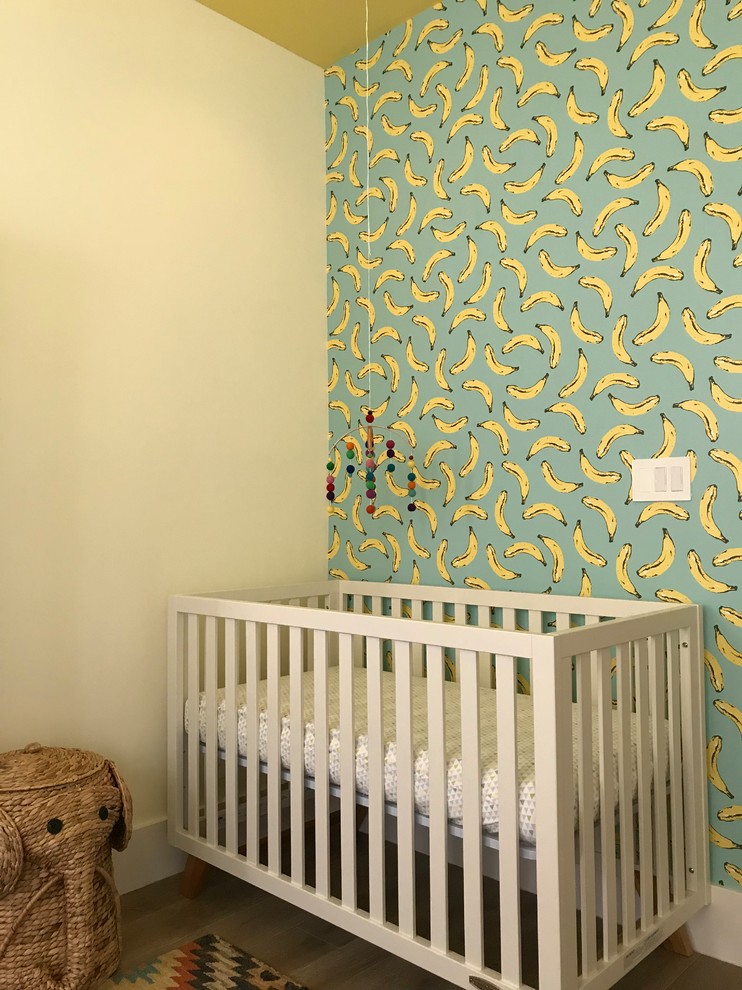 Modelo de habitación de bebé neutra grande con paredes amarillas, suelo de madera en tonos medios y suelo marrón