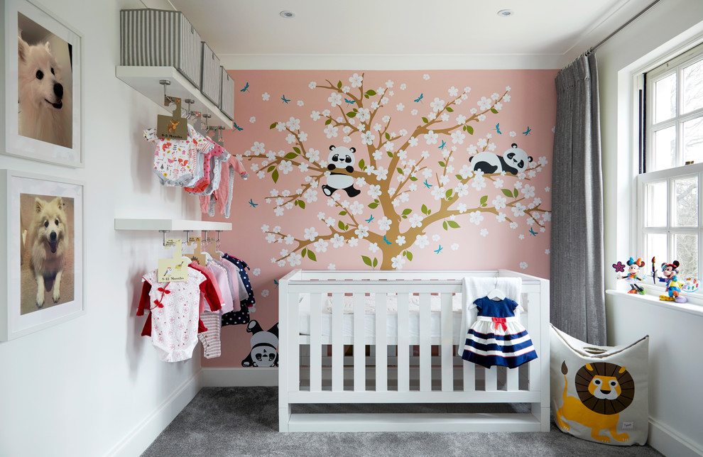 This is an example of a medium sized contemporary nursery for girls in Kent with pink walls, carpet, grey floors and a feature wall.