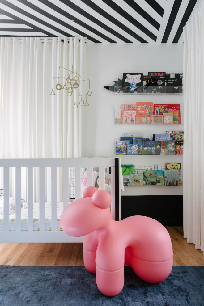 Ejemplo de habitación de bebé actual con paredes blancas, suelo de madera en tonos medios, suelo marrón y papel pintado